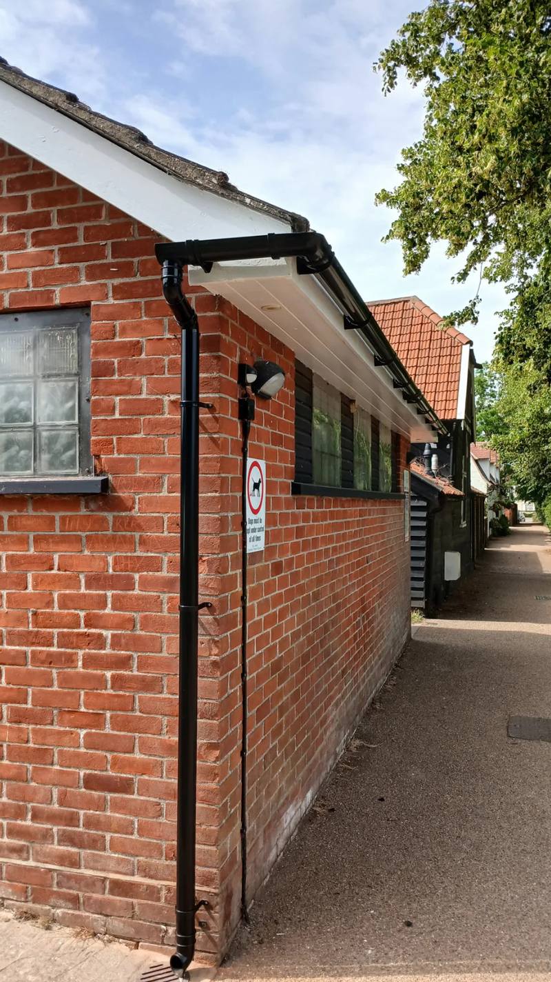 New white fascia and soffit with black guttering and downpipe on a brick building